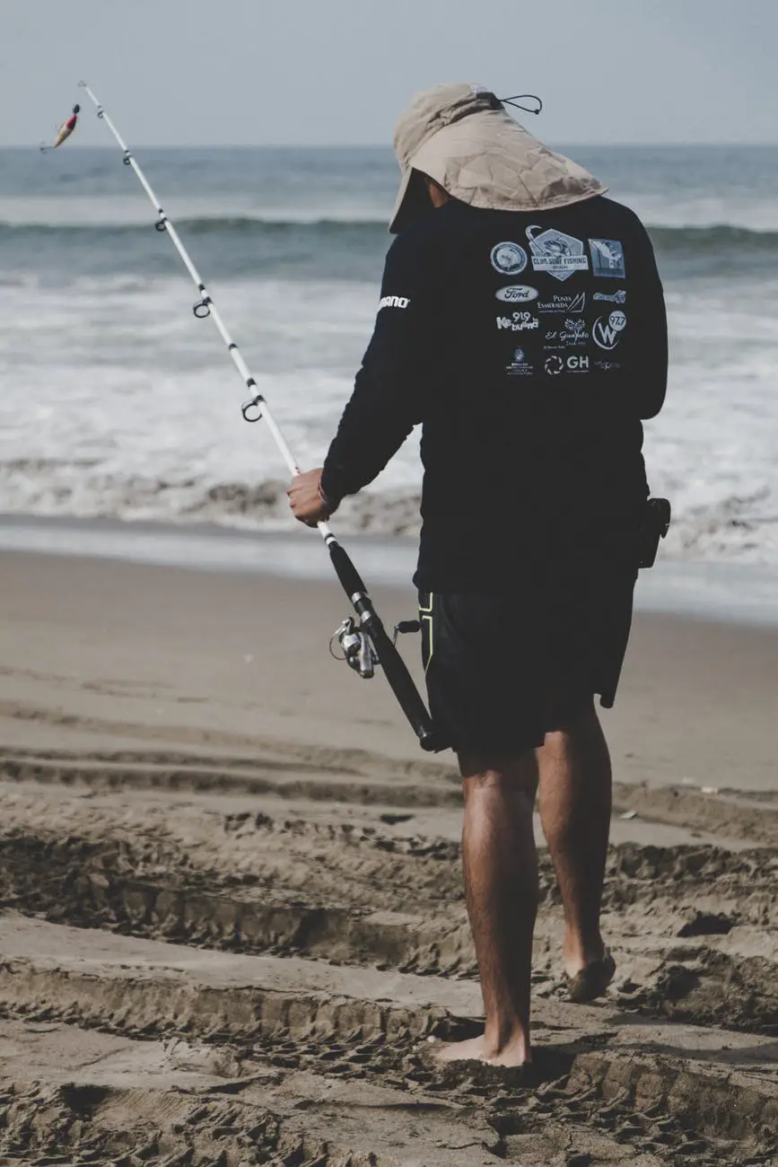 man in black long sleeved top holding white fishing rod near beach