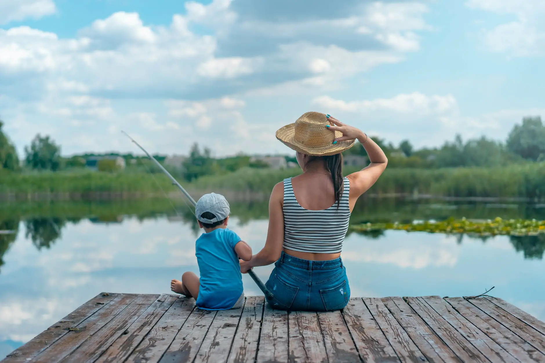 woman and boy sitting on dock holding fishing rod