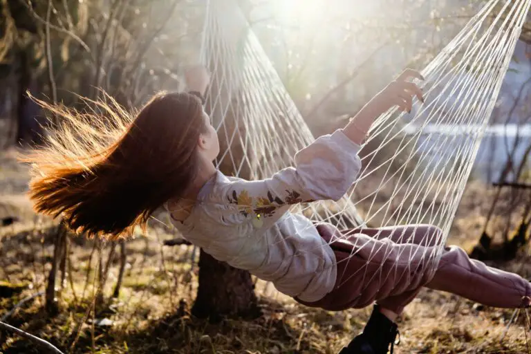 girl with long red hair sitting in hammock and swinging