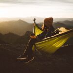 unrecognizable woman sitting in hammock above mountains